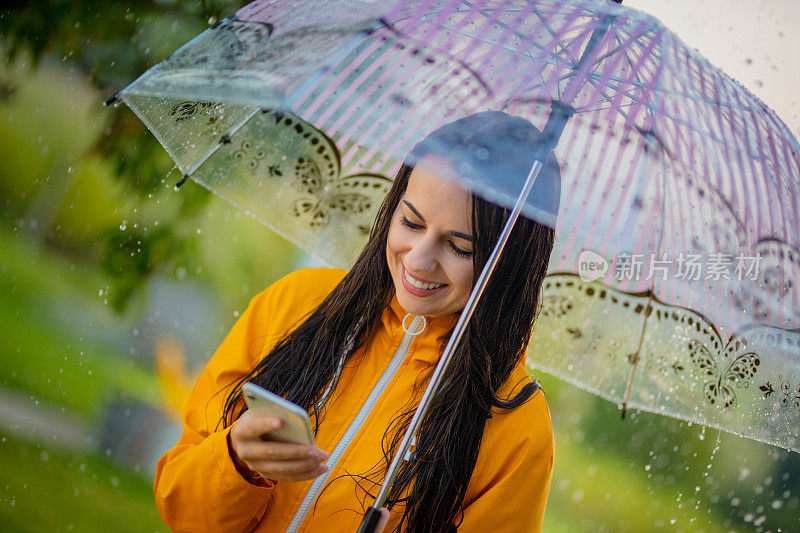 一个年轻的女人在雨中穿着黄色雨衣使用手机的肖像