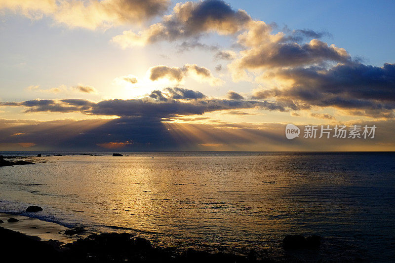 在海上的日落天空中，阳光从阴沉的云层中照射下来