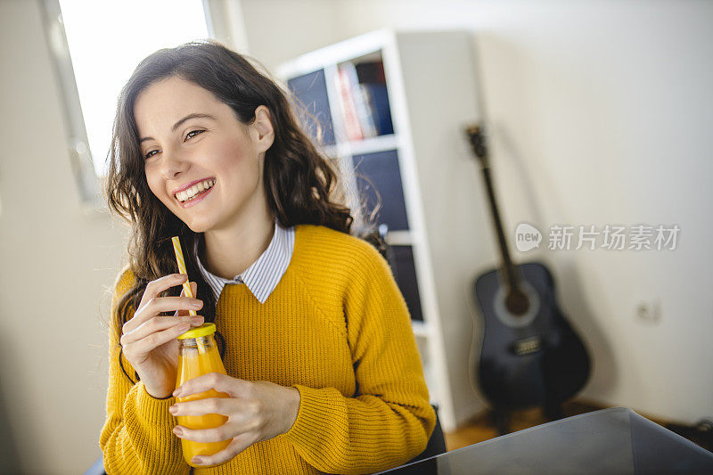 年轻女子喝着橙汁在家工作
