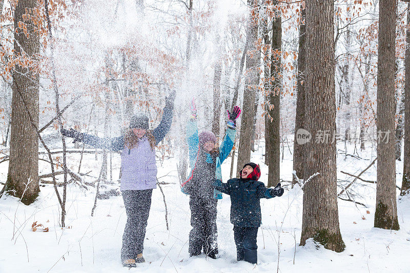 三个孩子在冬天的树林里玩扔雪