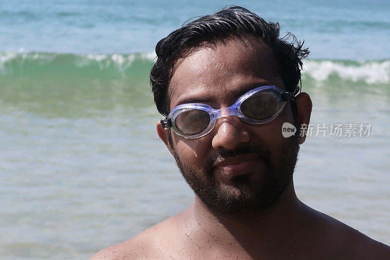 印度果阿巴洛勒姆海滩，一名印度男子在海滩度假，站在印度洋上戏水，戴着护目镜笑得很开心