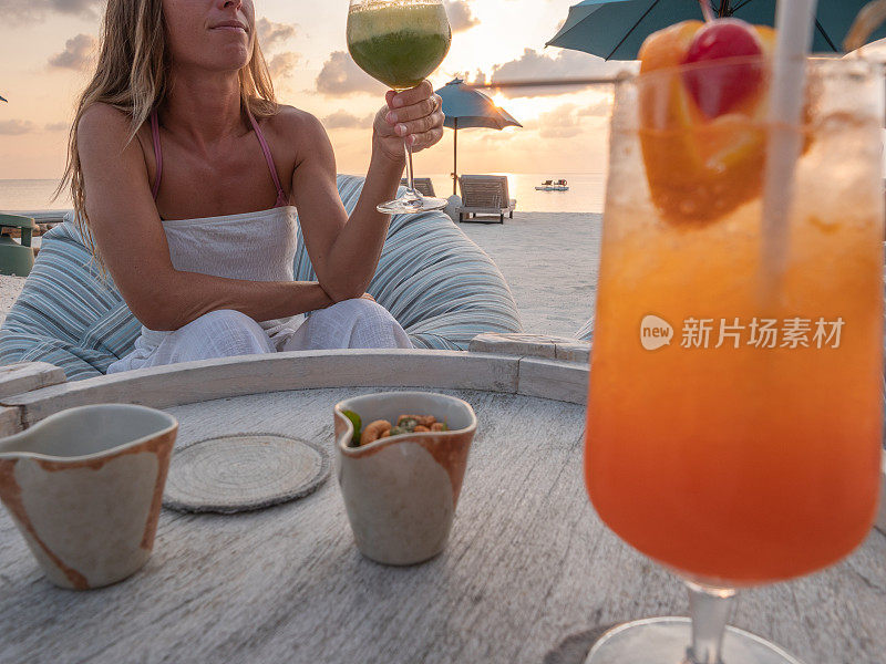 日落时分在热带海滩上喝鸡尾酒的女人
