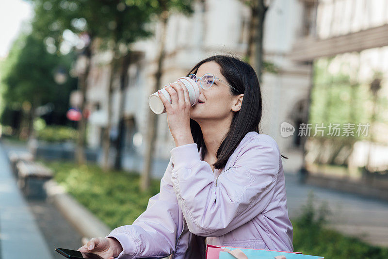 年轻女子用可重复使用的杯子喝咖啡，享受城市生活