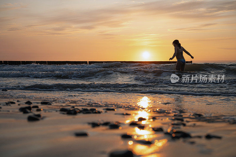 日落时分，小女孩站在波罗的海的波浪中