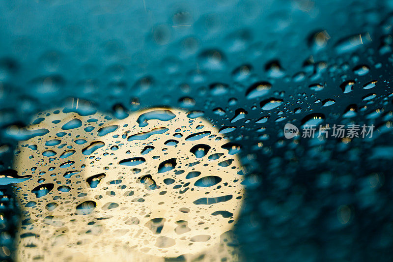 雨点落在挡风玻璃上，车头灯在背景中