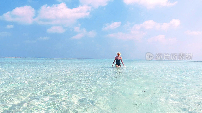 性感的金发女人走过马尔代夫的浅水