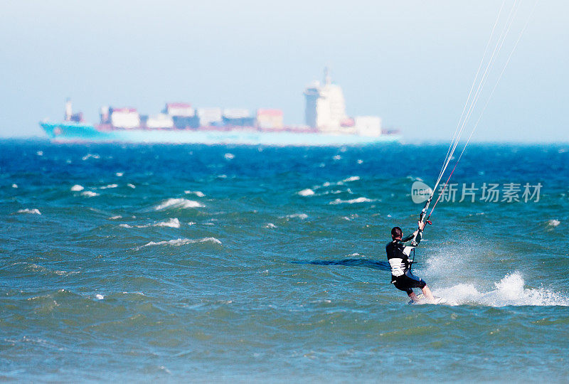 在波涛汹涌的海面上玩风筝，背景是集装箱船