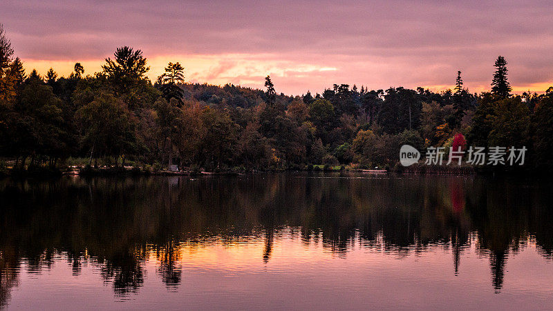 秋天的夕阳和林地倒映在静静的湖面上