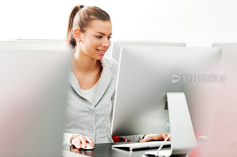 微笑的女学生在计算机实验室使用计算机。