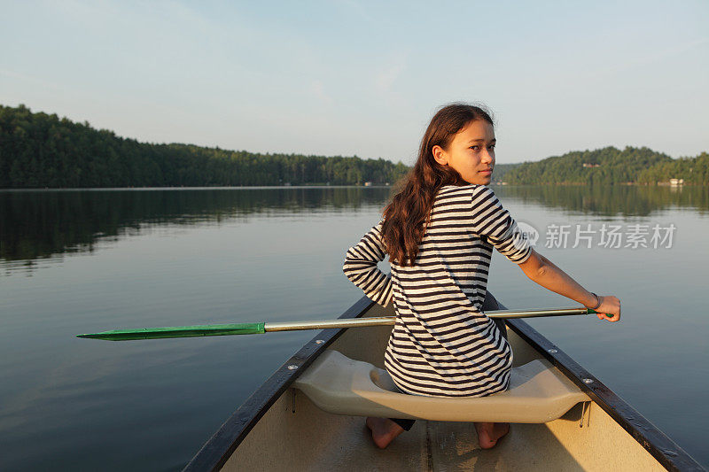 年轻女孩在平静的湖面上划着独木舟