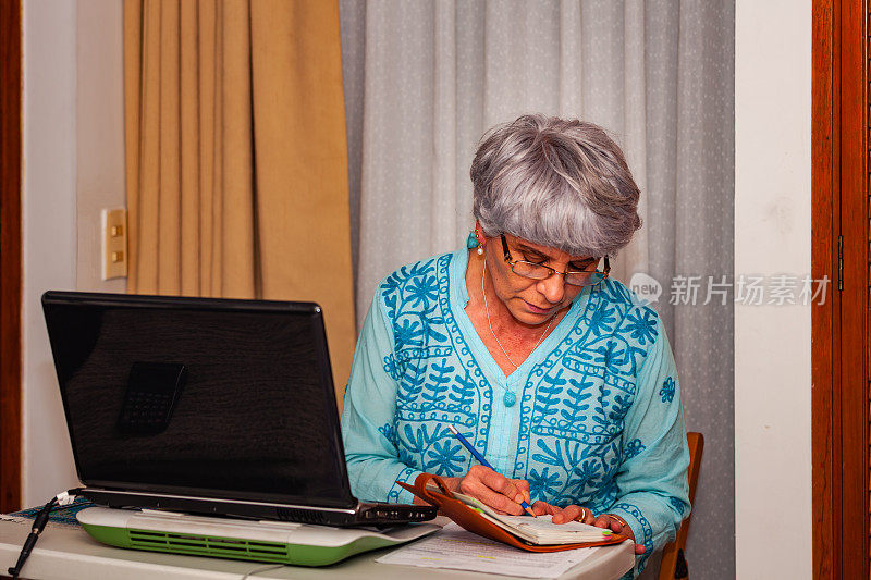 西班牙裔银发老太太在家用笔记本电脑工作