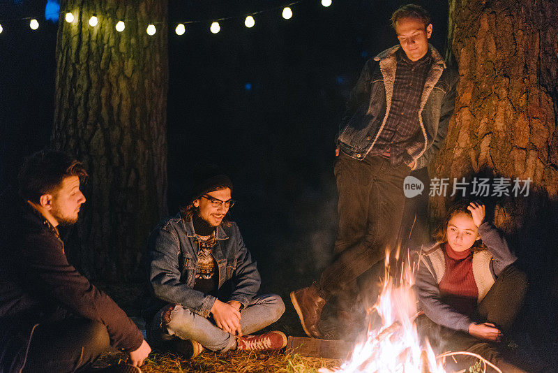 朋友们坐在森林里靠近露营车的篝火旁