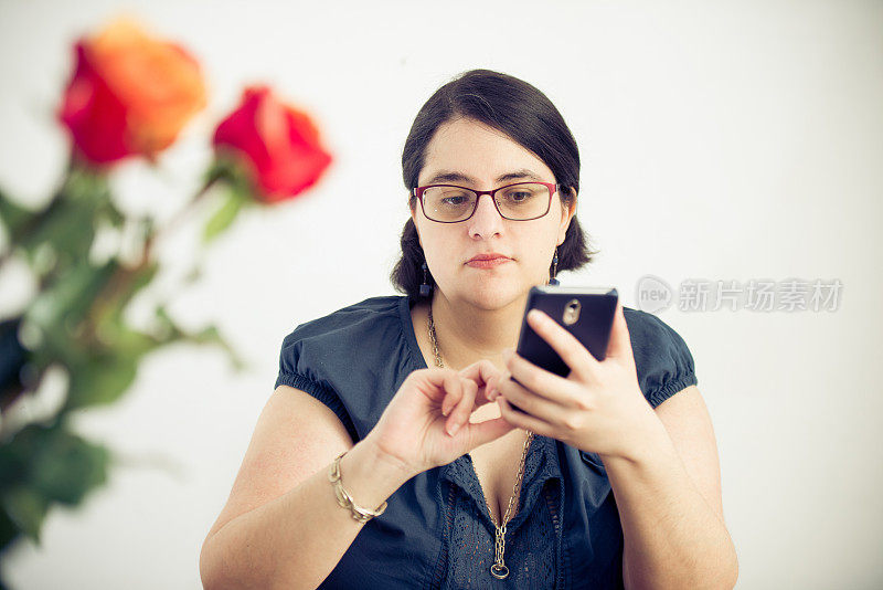 戴眼镜的女人在桌子后面用智能手机