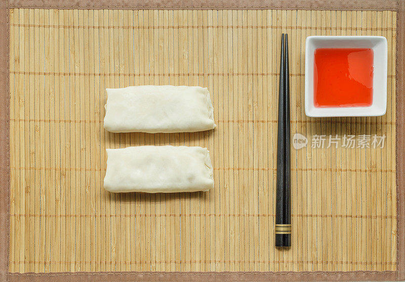 木筷子，春卷和糖醋酱竹席背景。