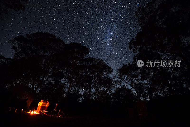 一群露营者围着篝火站着，上面闪烁着明亮的星星