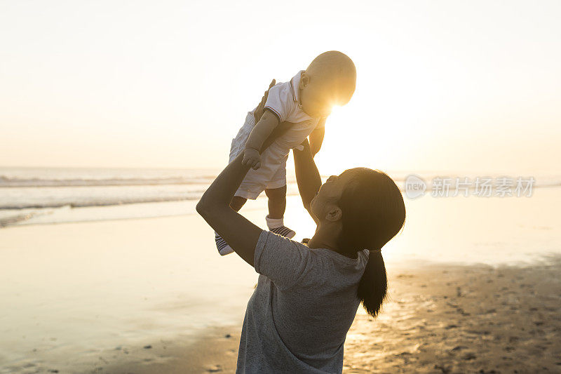 夕阳西下的海滩上，母亲抱着她的小儿子