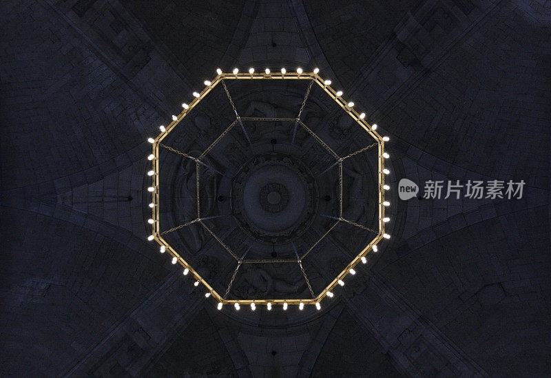 底部的观点，瓷砖圆顶天花板碎片与吊灯闪烁在暮色。具有多边形几何结构的抽象建筑背景。