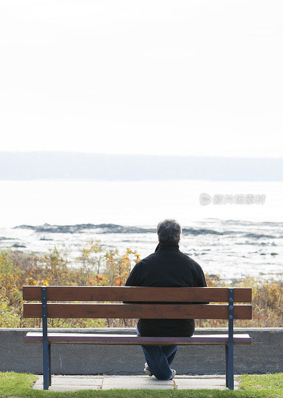 一个成熟的男人坐在公园长椅上俯瞰着河流。