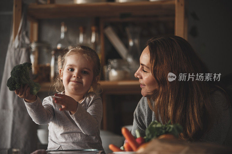 小女孩抱着花椰菜，和妈妈一起做饭