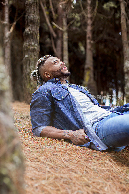 一个扎着辫子的黑人，躺在森林中央的地上，仰望着大自然，欣赏大自然。