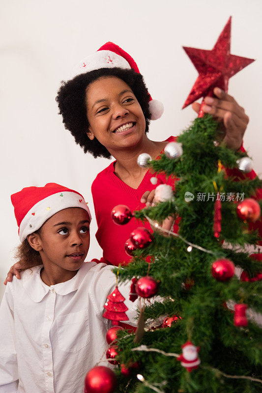 黑人妇女微笑着和她的孩子把圣诞装饰品放在圣诞松树上