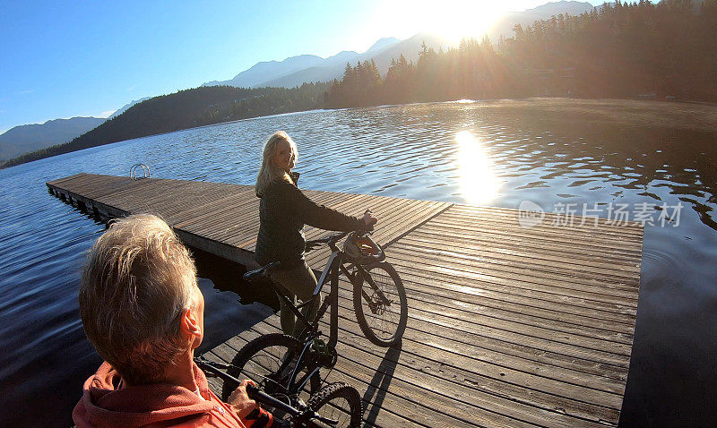 一对夫妇在日出时沿着湖边的码头骑自行车
