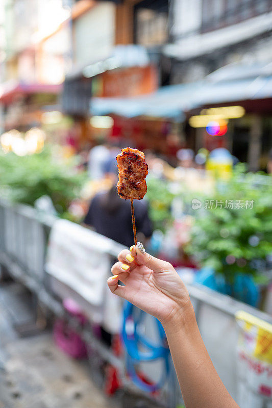 一名女游客在街上手拿泰国烤猪肉棒