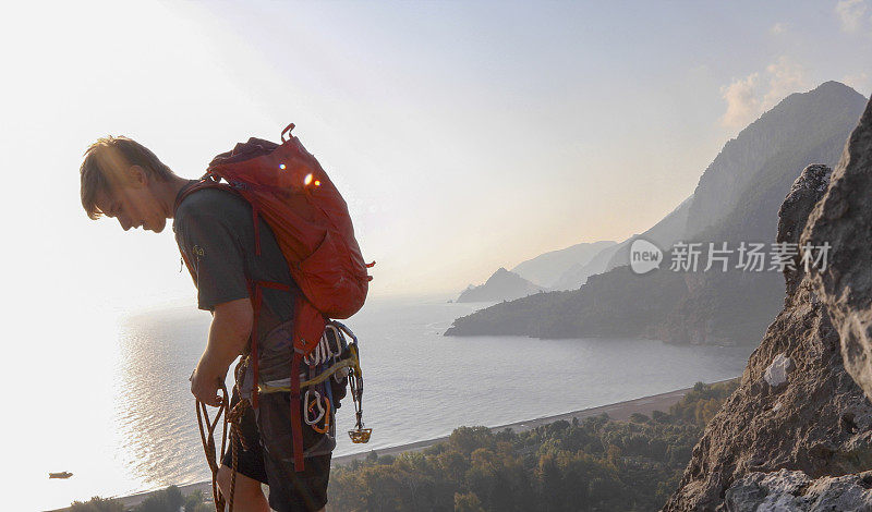 男性登山运动员在日出时爬上岩石顶峰