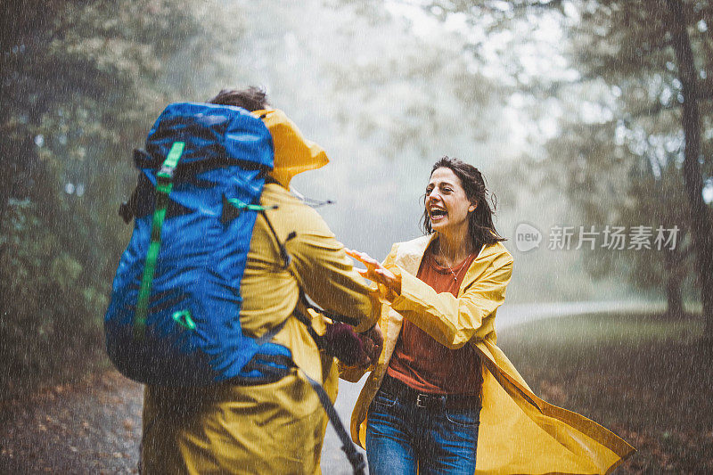 穿着黄色雨衣的快乐夫妇在雨天的森林里玩耍。