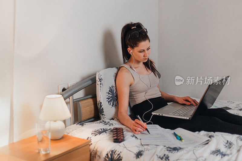 被隔离的年轻女子坐在床上拿着笔记本电脑