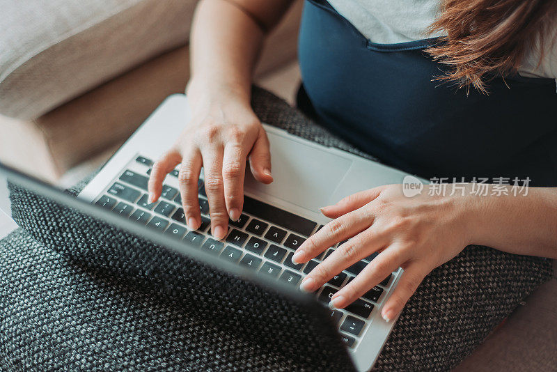 特写的亚洲华人女性坐在沙发上使用笔记本电脑和在家工作