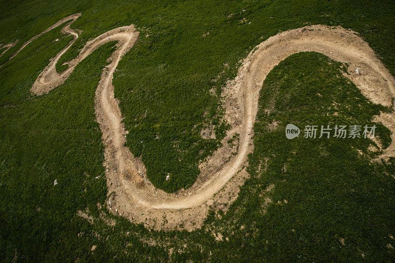 山地车道蜿蜒穿过开阔的绿色草地的鸟瞰图