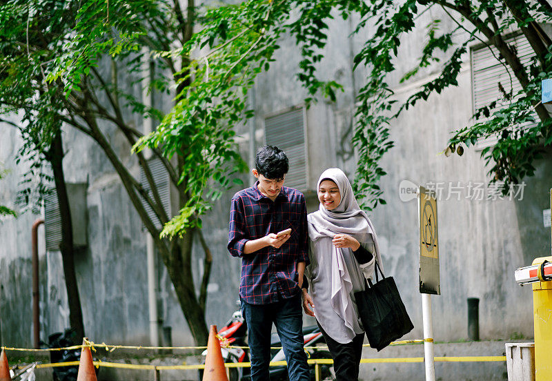 年轻美丽的穆斯林夫妇看手机一起走时