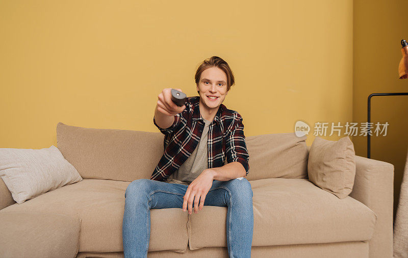 年轻的男子拿着遥控器坐在沙发上，结束了隔离的概念