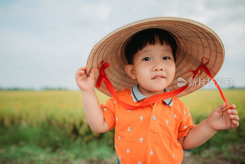 带着传统藤帽的亚洲华人男孩站在稻田边的肖像