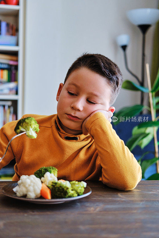 孩子对不得不吃蔬菜很不高兴。他的盘子里有许多蔬菜。他讨厌蔬菜。