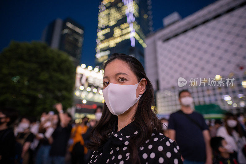 一名年轻女子戴着保护面罩，晚上站在涉谷路口