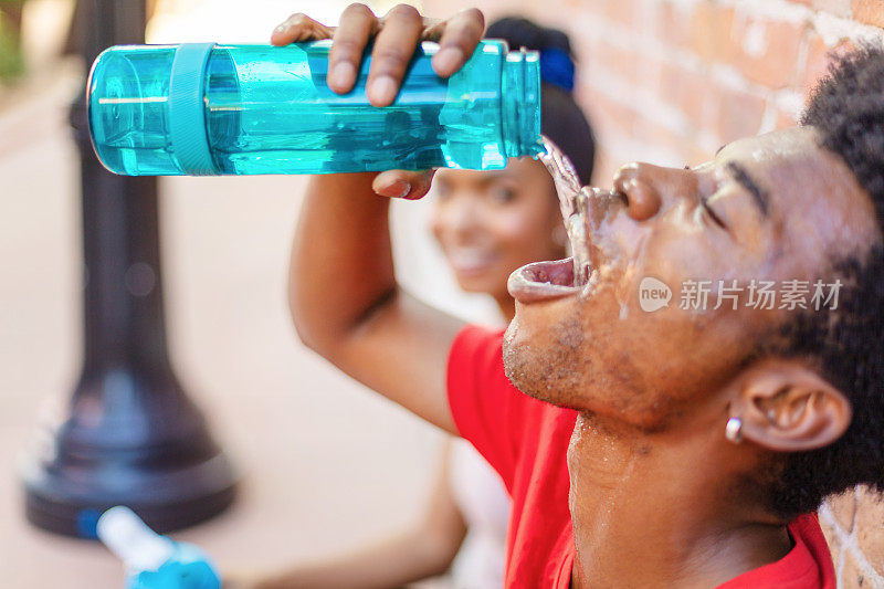 千禧年男性和Z一代女性在炎热的夏日里锻炼，拿着水瓶补水