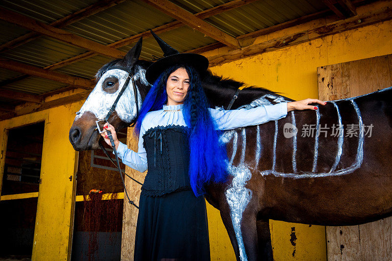 万圣节庆典，一个穿着女巫服装的年轻女孩站在一匹画着骷髅的马旁边