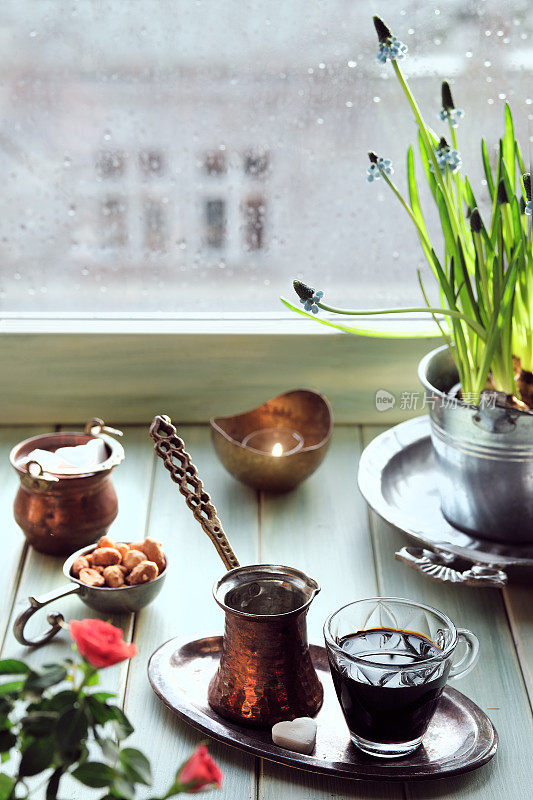 传统土耳其铜咖啡壶的东方咖啡，窗台上有花。木窗与风信子花盆。寒冷的春天雨天。舒适的场景，hygge概念