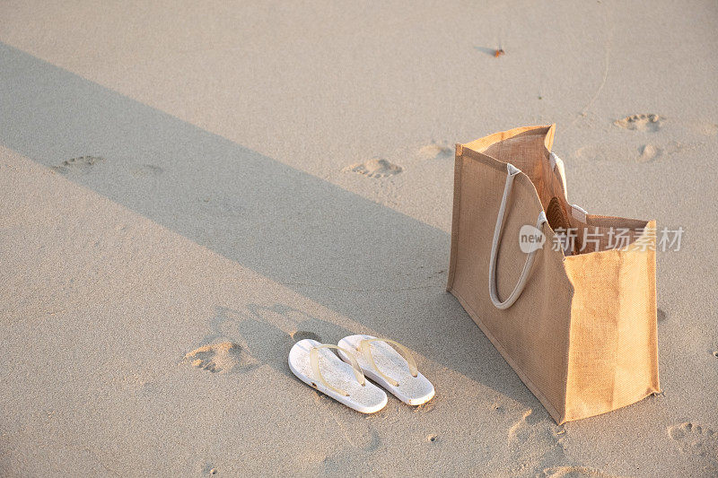 一个包和一双拖鞋在热带的白色沙滩上