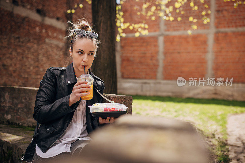 年轻女子在公园里吃着新鲜的有机沙拉，喝着橙汁