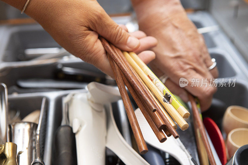 一个女人的手握木筷子的特写，把它们放进厨房的抽屉里