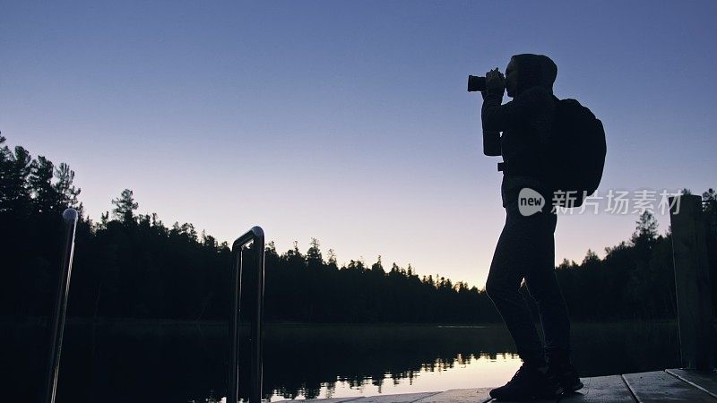 剪影旅行者拍摄风景在森林，河流。木材码头。一个女人拍了漂亮的黑魔法夜景。女孩用相机拍照。