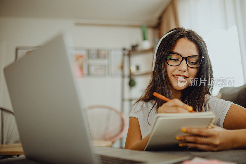 一位年轻的女学生坐在沙发上使用笔记本电脑耳机学习