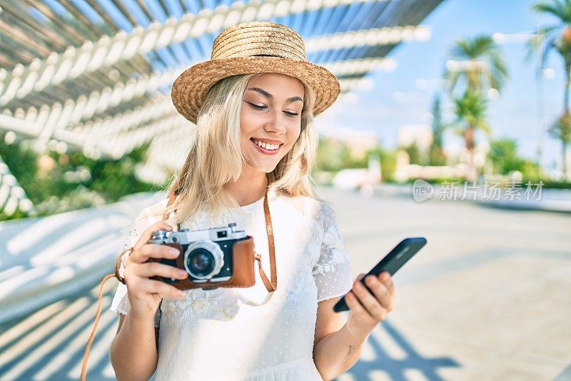 年轻的白人旅游女孩在城市的街道上使用智能手机和老式相机。
