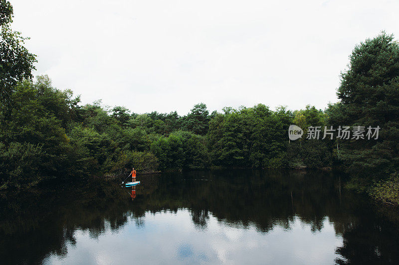 一个穿橘色衣服的女人在森林深处的湖边玩冲浪