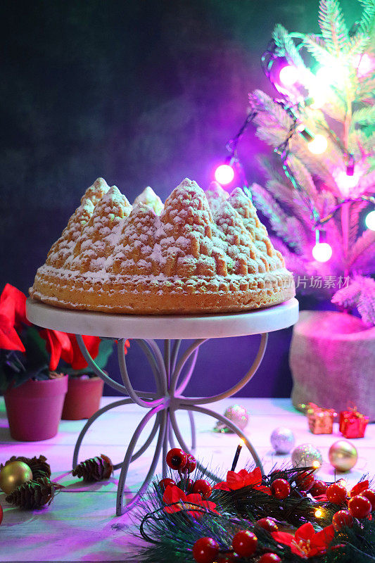 特写图像自制，圣诞树形状，柠檬细雨Bundt蛋糕在白色，大理石和金属蛋糕架周围的圣诞装饰，柠檬味的环海绵覆盖着糖霜，照亮的童话灯