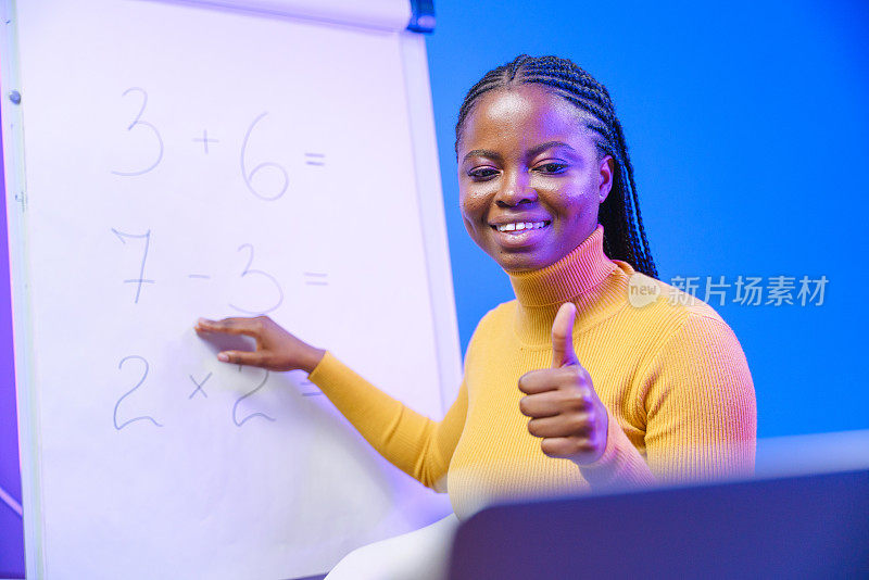 在网上数学课上，一位迷人的深色皮肤的年轻教师在她的笔记本电脑上展示“竖起大拇指”