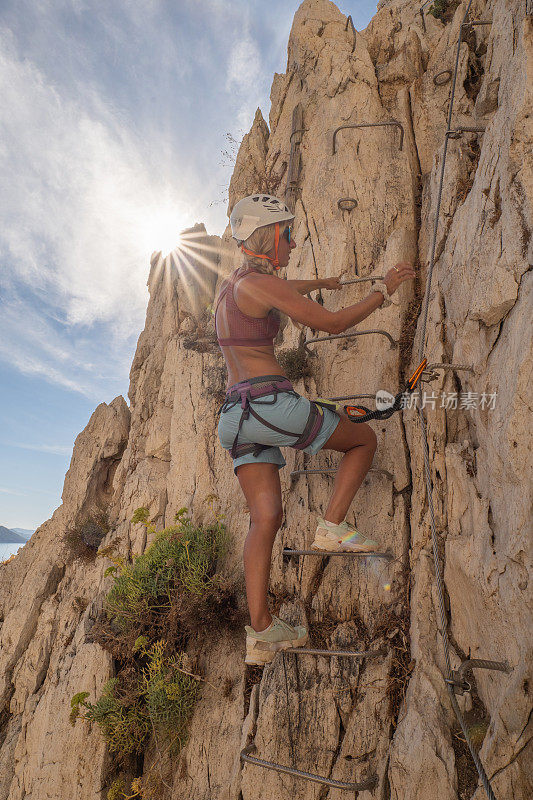 女性攀岩者爬上梯子到达岩石顶部的低角度视图